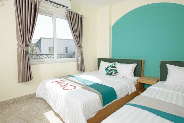 Une chambre d’hôtel avec deux lits, une fenêtre avec des rideaux, un mur d’accent de couleur turquoise et une vue sur les bâtiments environnants.