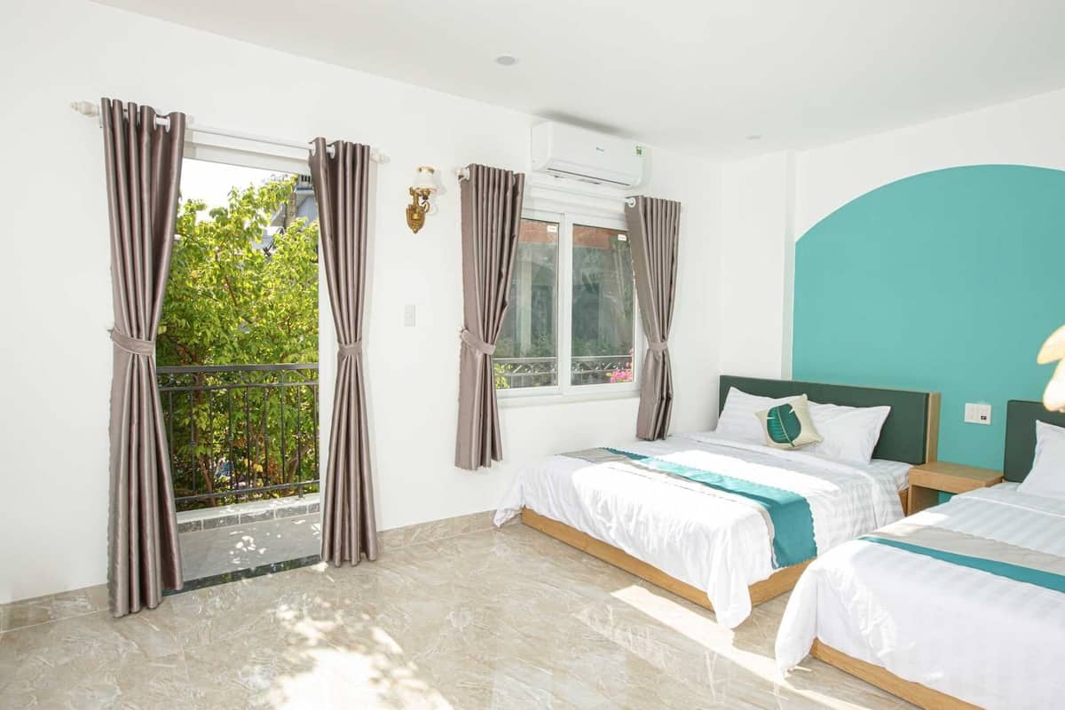 A hotel room with two beds, a window with curtains, a balcony, and a teal accent wall.