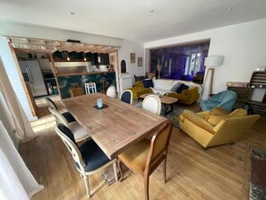 A modern living room with a wooden dining table, yellow sofas, and a large window with a view. - Maison Estagnole (Estaing)