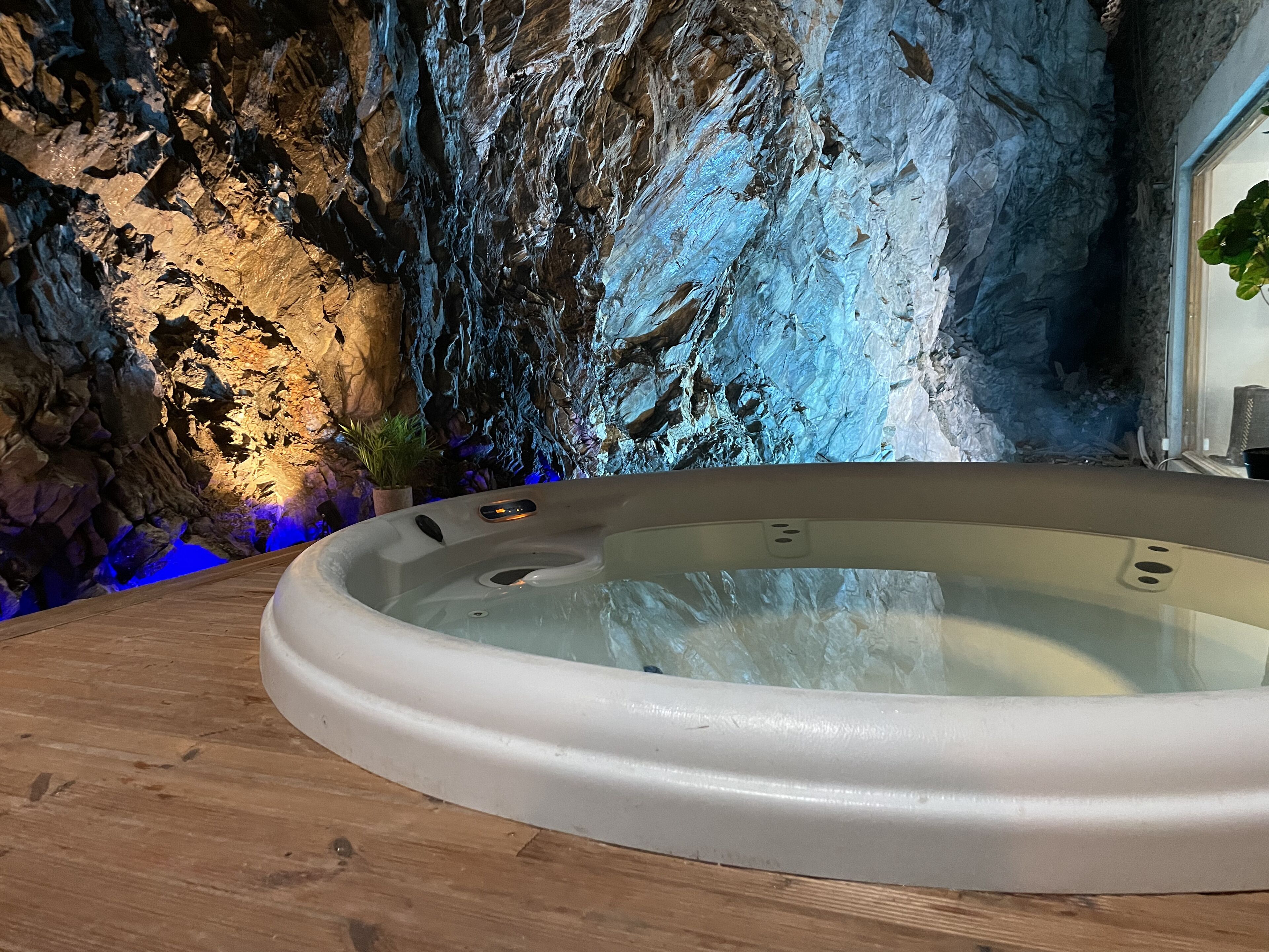 A hot tub in a room with a rocky wall and a wooden floor.
