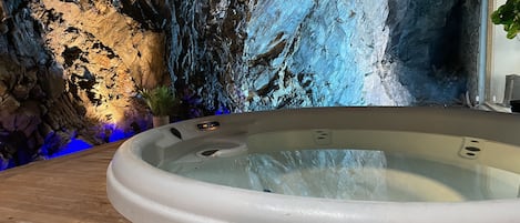 A hot tub in a room with a rocky wall and a wooden floor.