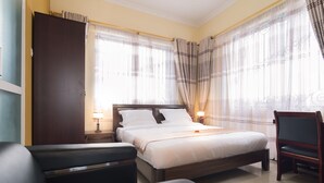 Ein Hotelzimmer mit Bett, Sessel, Nachttisch und einem Fenster mit Vorhängen.