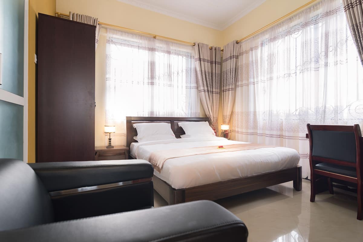 Une chambre d’hôtel avec un lit, une chaise, une table de chevet et une fenêtre avec des rideaux.