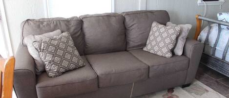 A brown sofa with patterned cushions in a room with a tiled floor and a patterned rug.