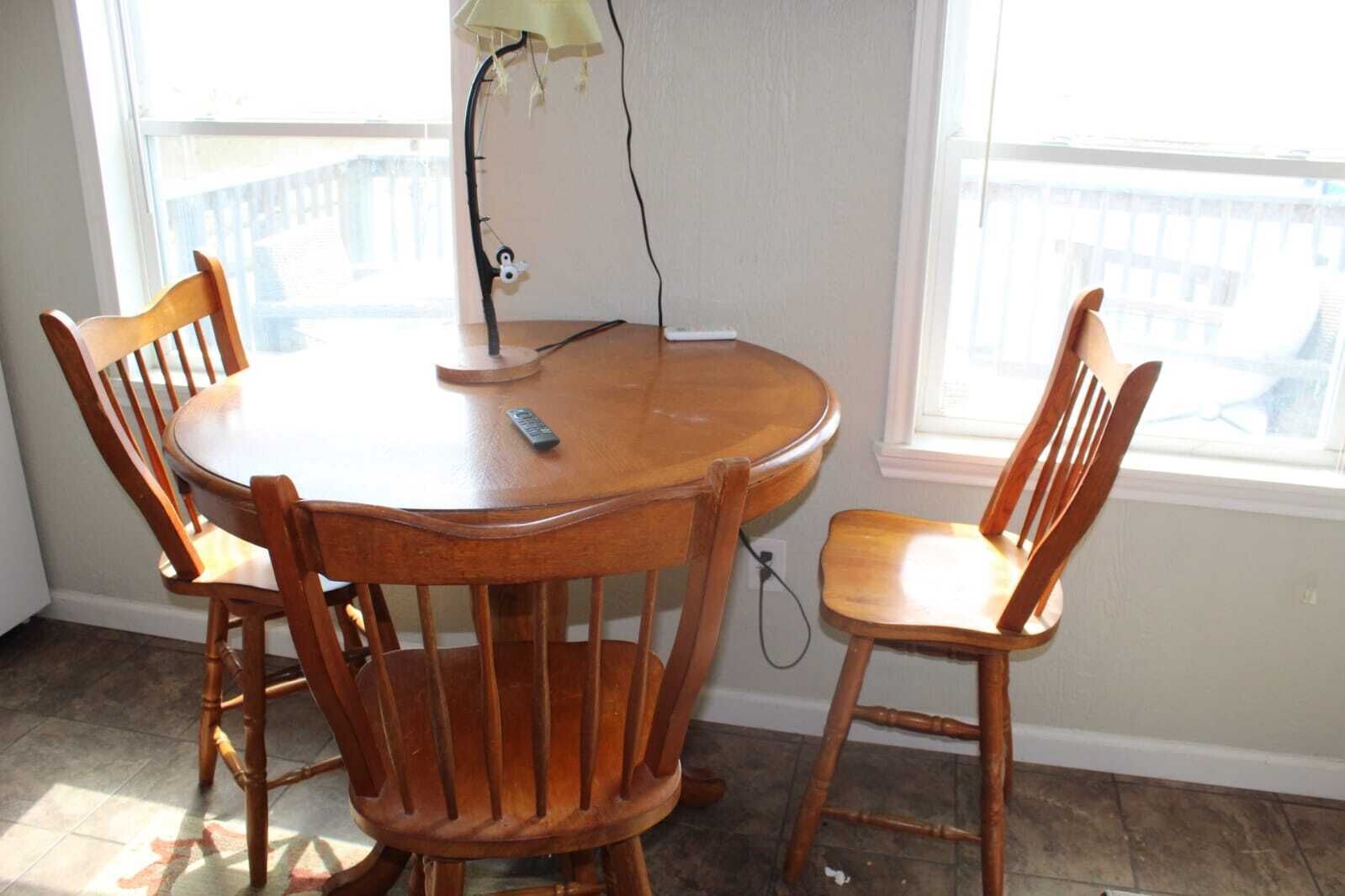 A round wooden dining table with four chairs, a lamp, and a remote control on the table.