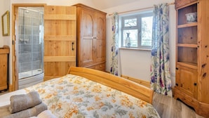 A bedroom with a wooden bed, a wooden wardrobe, a wooden cabinet, and a window with floral curtains. - The Old Greenhouse - UK45328 (Wragby)