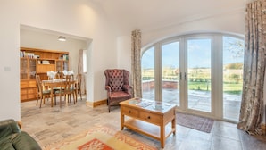 A spacious living room with a large window, a dining area with a wooden table and chairs, and a leather sofa. - The Old Greenhouse - UK45328 (Wragby)
