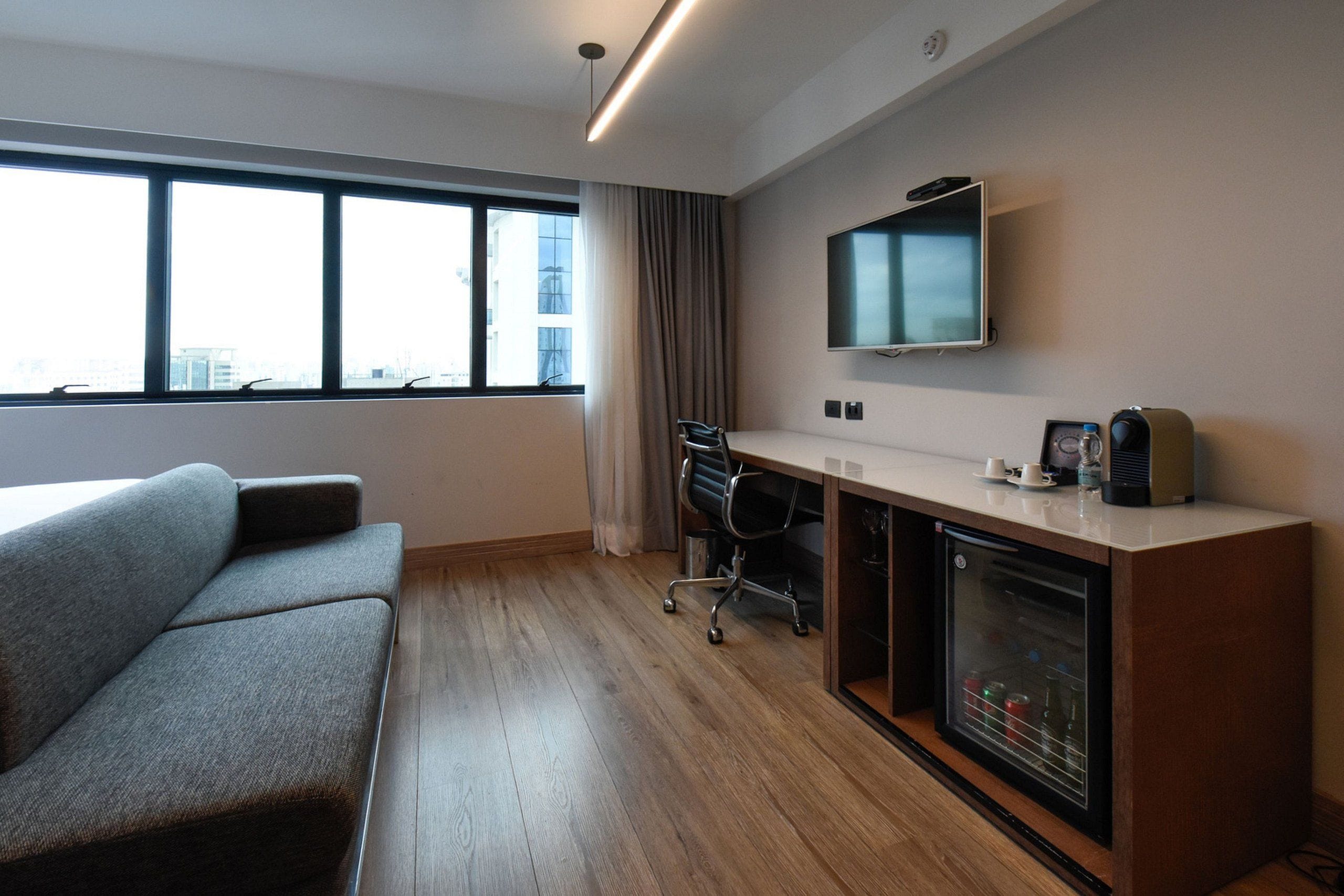 Quarto de hotel moderno com sofá, escrivaninha com computador, televisão de tela plana e minibar.