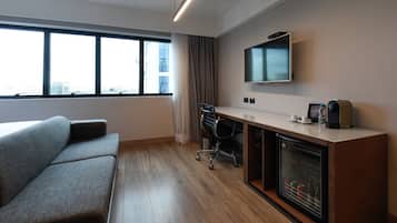 Quarto de hotel moderno com sofá, escrivaninha com computador, televisão de tela plana e minibar.