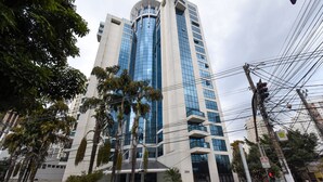 A modern high-rise building with a glass facade, surrounded by palm trees and a pedestrian crossing.
