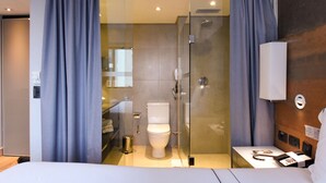 A modern hotel room with a glass shower enclosure, a white toilet, and a bedside table with a phone and a lamp. - Elegance Suites Ibirapuera (São Paulo)
