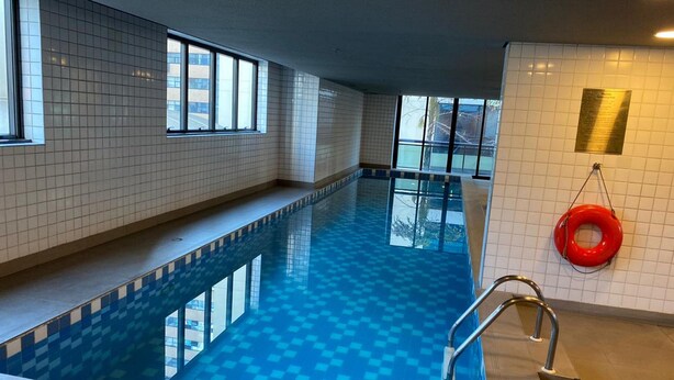 An indoor swimming pool with clear blue tiles, a lifebuoy, and a window providing natural light. - Elegance Suites Ibirapuera (São Paulo)