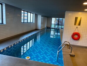 Une piscine intérieure aux carreaux bleu clair, équipée d’une bouée de sauvetage et d’une fenêtre laissant entrer la lumière naturelle.
