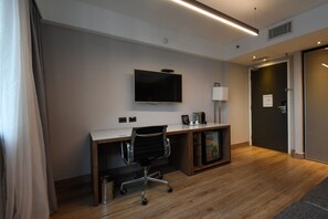 Une chambre d’hôtel avec un bureau en bois, un téléviseur à écran plat fixé au mur, un petit meuble et une porte sur le côté droit.