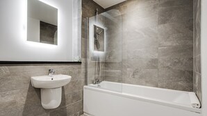 Et moderne badeværelse med et glasafskærmet brusebad, en hvid vask og et badekar.