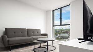 En moderne stue med en grå sofa, et lille rundt bord og et fjernsyn på et hvidt skrivebord.