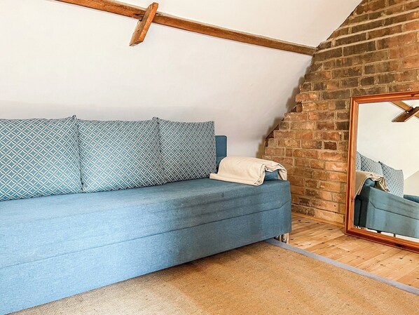 Un canapé bleu avec des coussins à motifs, un plafond avec des poutres en bois, un mur en briques et un miroir sur le côté droit.