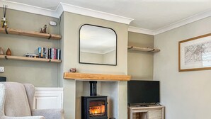Un salon chaleureux avec une cheminée, un fauteuil confortable, une table basse en bois et un meuble pour la télévision.