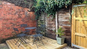 Une terrasse en bois avec une table et des chaises, un pot de fleurs et une porte en bois.