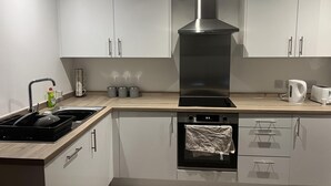 Eine moderne Küche mit weißen Schränken, einer Edelstahl-Dunstabzugshaube, einem eingebauten Backofen und einem Wasserkocher auf der Arbeitsplatte.