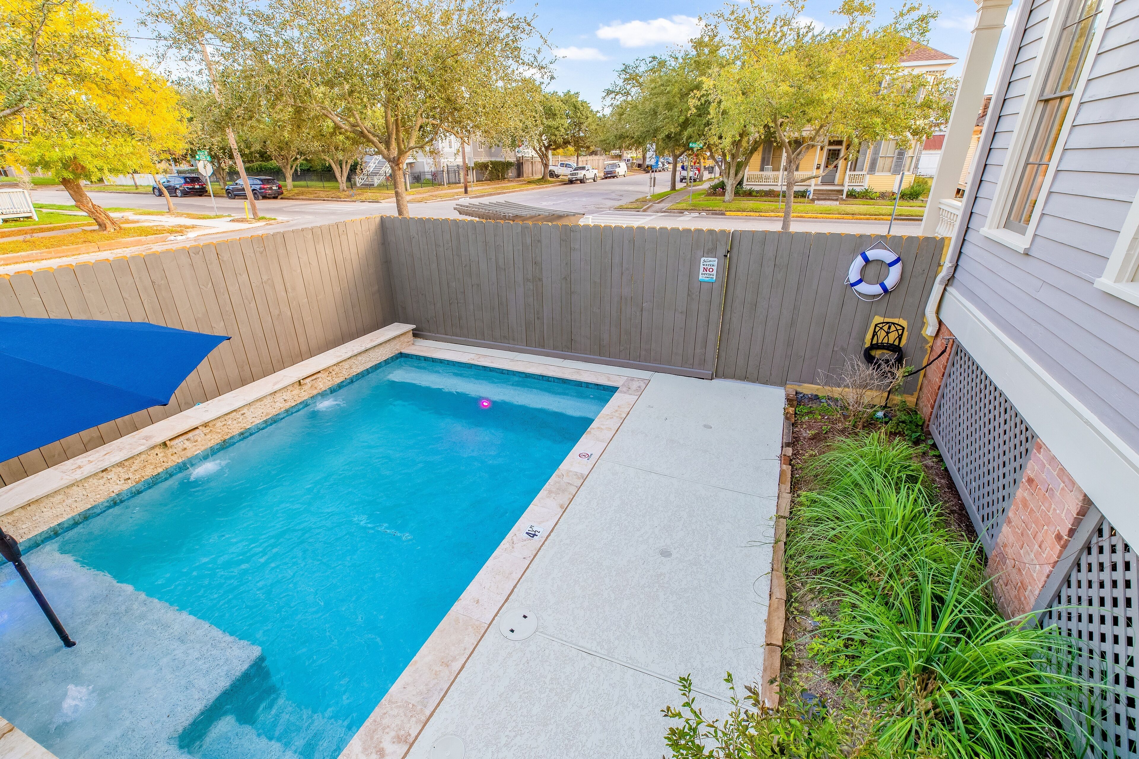 A small rectangular pool with a blue umbrella, surrounded by a wooden fence and a brick wall.