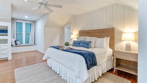 Una camera da letto con un letto, comodini, una finestra con tende, una ventola a soffitto e una panca integrata con cuscini.