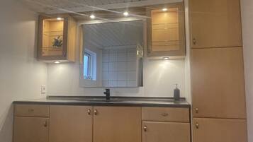 A bathroom with a black countertop, wooden cabinets, a mirror, and a window.