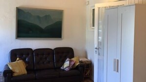 Una habitación con techo de madera, un sofá marrón oscuro con cojines, un armario blanco y un cuadro de montañas en la pared.