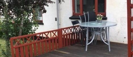 A house with a wooden deck, a glass table with chairs, and a red railing.
