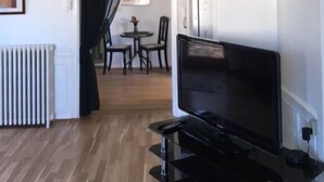 Una sala moderna con un televisor de pantalla plana sobre un mueble, un radiador y un comedor con una mesa y sillas.