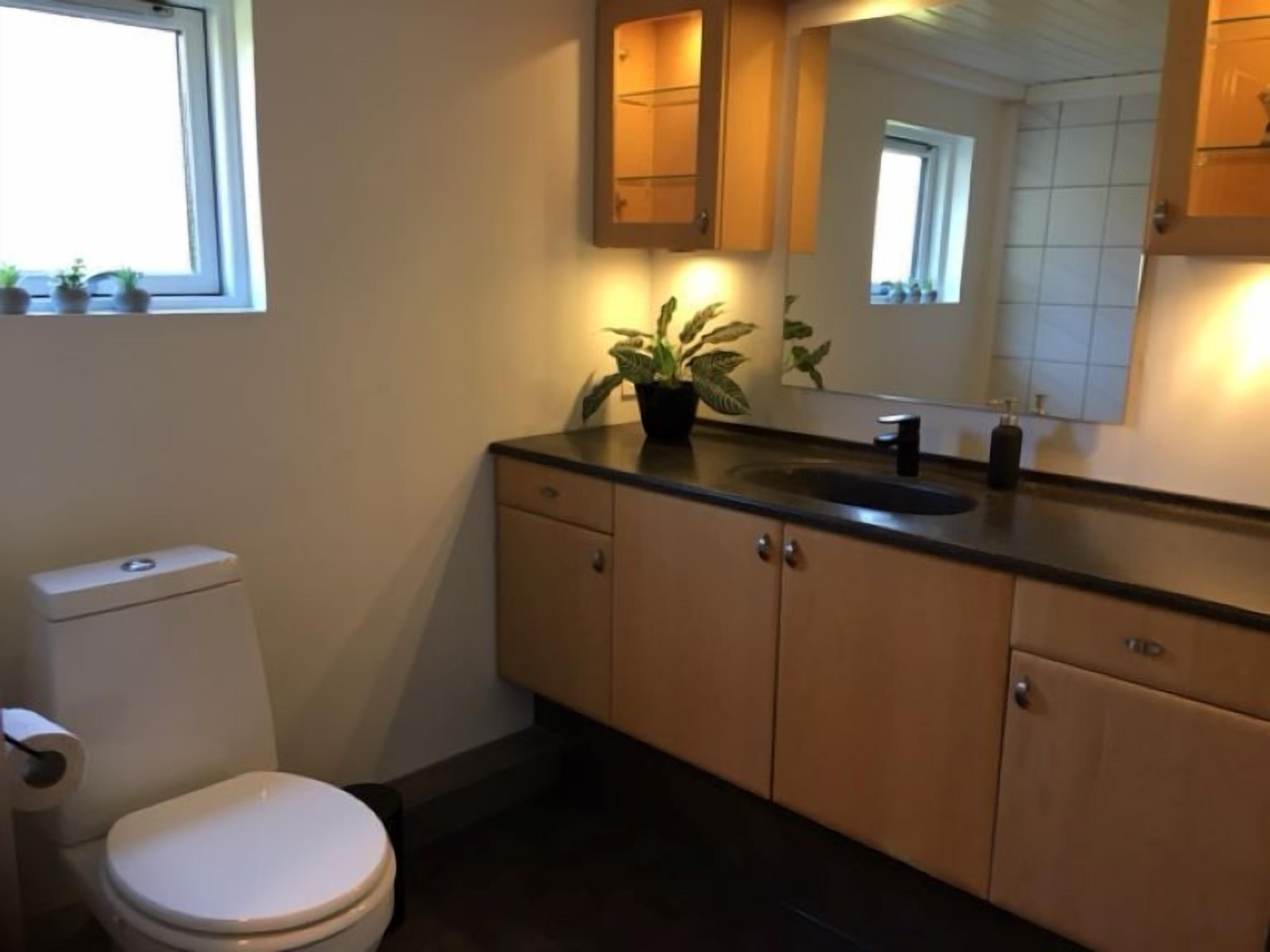 A bathroom with a toilet, sink, cabinets, and a mirror.