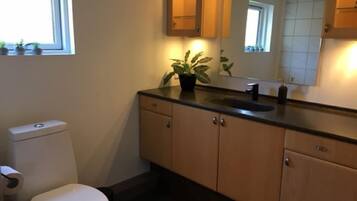 A bathroom with a toilet, sink, cabinets, and a mirror.