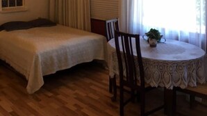 Una habitación con techo de madera, una cama con colcha blanca, una mesa redonda con mantel de encaje y una planta en maceta.