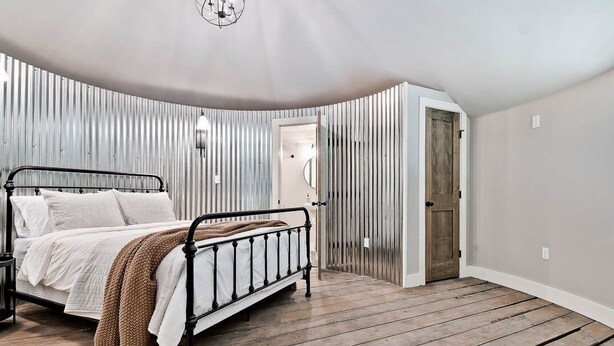 A bedroom with a metal bed frame, a wooden floor, and a slanted ceiling. - HJ's Silos (Fayetteville)