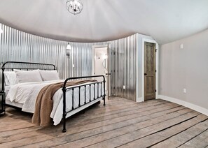 A bedroom with a metal bed frame, a wooden floor, and a slanted ceiling. - HJ's Silos (Fayetteville)