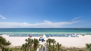 A beach with rows of umbrellas and beach chairs, a pier in the distance, and palm trees in the foreground. - Gulf View Family Getaway, Amazing Pool, Short walk to Beach & Pier Park (Panama City Beach)