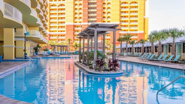 A swimming pool with a gazebo, lounge chairs, and a large hotel building in the background. - Gulf View Family Getaway, Amazing Pool, Short walk to Beach & Pier Park (Panama City Beach)