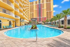 A hotel pool area with a circular pool, lounge chairs, and a large building in the background.