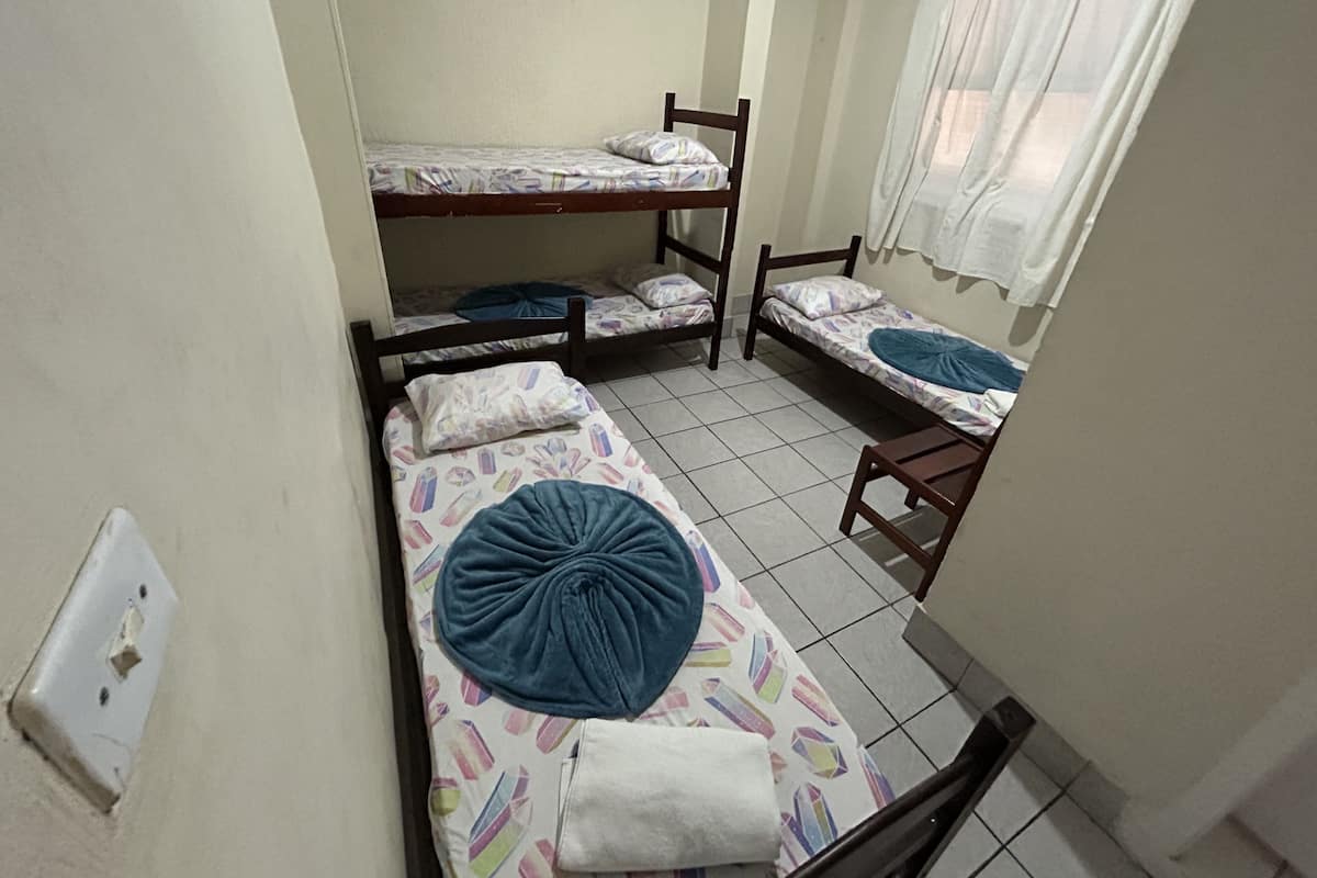 A dormitory room with three bunk beds, a small wooden table, and a window with curtains.