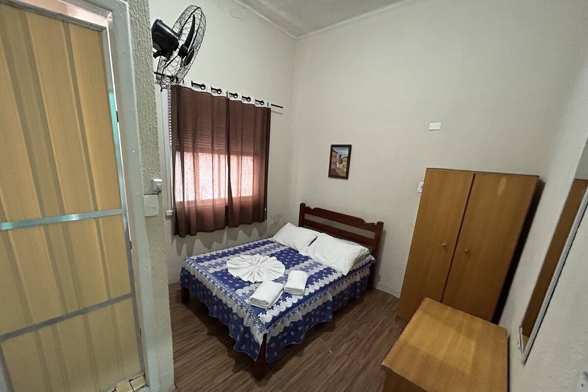 A bedroom with a bed, a wooden wardrobe, a fan, and a door.