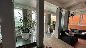 A spacious indoor area with a black sofa, a dining table with chairs, and several potted plants. - Pousada da Praia (Sao Vicente)