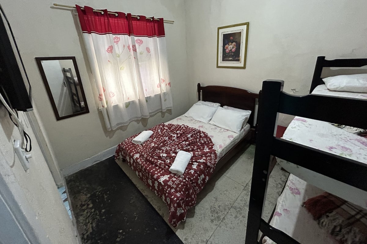 A small, simple room with a single bed, a wooden bunk bed, a mirror, and a framed picture on the wall.