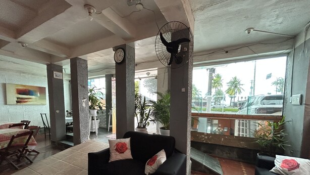 A hotel lobby with a black sofa, a clock, a fan, and a view of the street. - Pousada da Praia (Sao Vicente)