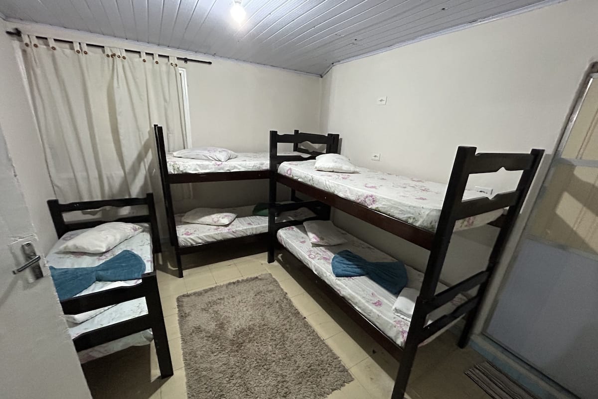 A bunk bed room with a wooden floor, a white curtain, and a small rug.