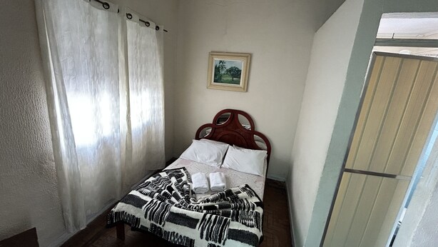 Une chambre à coucher avec un lit, des rideaux, un tableau encadré au mur et une porte en bois.