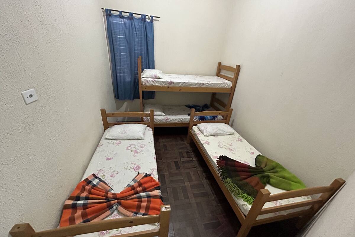A dormitory room with three wooden bunk beds, a blue curtain, and a wooden floor.