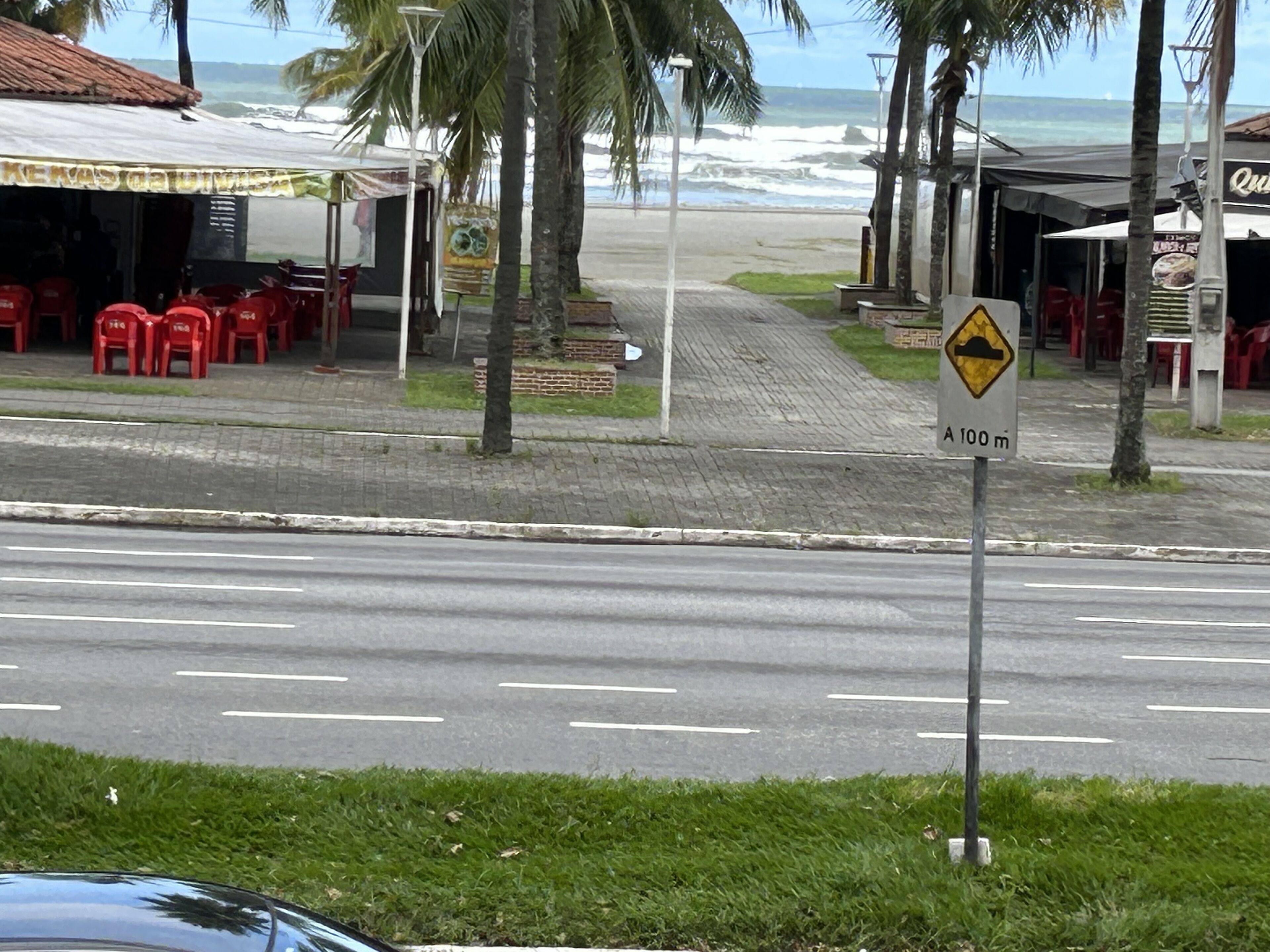 A coastal road with a speed bump warning sign, palm trees, and beachside restaurants.