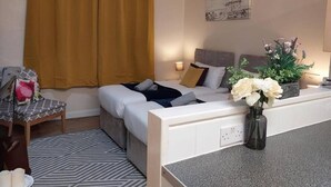 Quarto de hotel com cama, escrivaninha, cadeira, um vaso de flores e um quadro na parede.