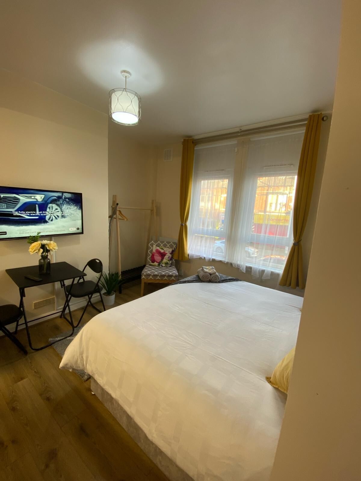 A hotel room with a bed, a desk with a TV, a chair, and a window with curtains.