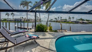 A poolside area with lounge chairs, a pool, and a view of a marina with boats and palm trees. - Beautiful views, watch the dolphins and tarpon swim by on the  lanai or dock! (Cape Coral)